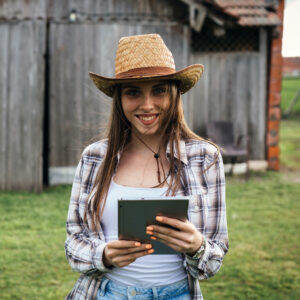 woman rancher standing in front of barn using digital tablet